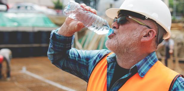 Oudere bouwvakker drinkt flesje water