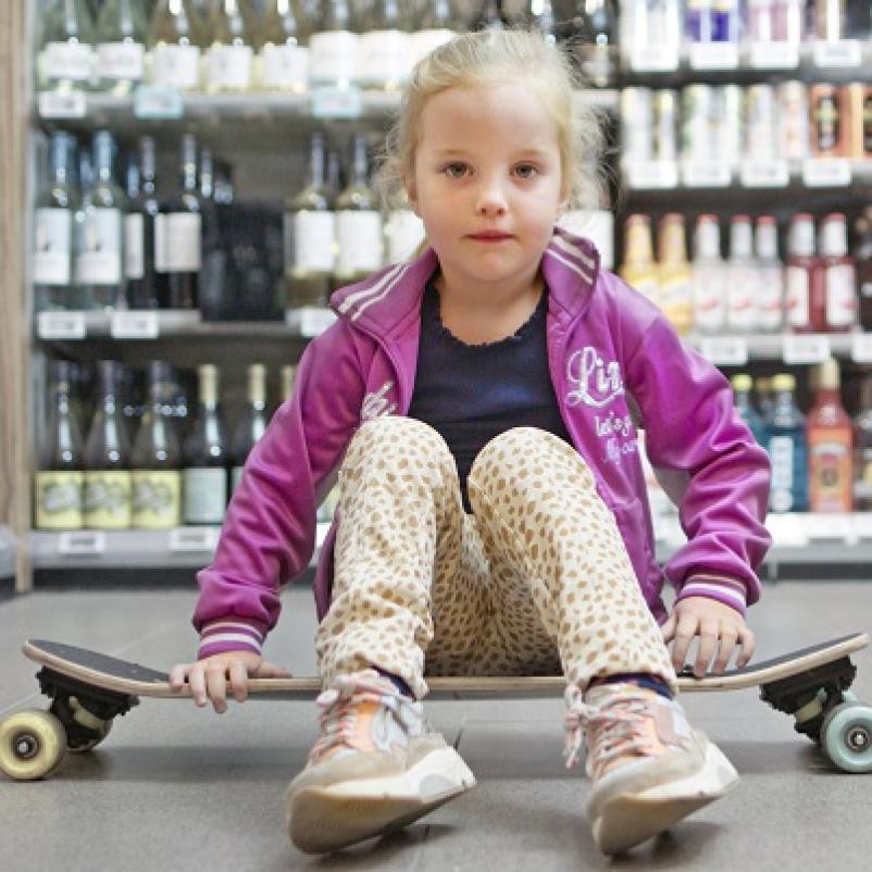 Jong meisje op skateboard voor drankschap supermarkt