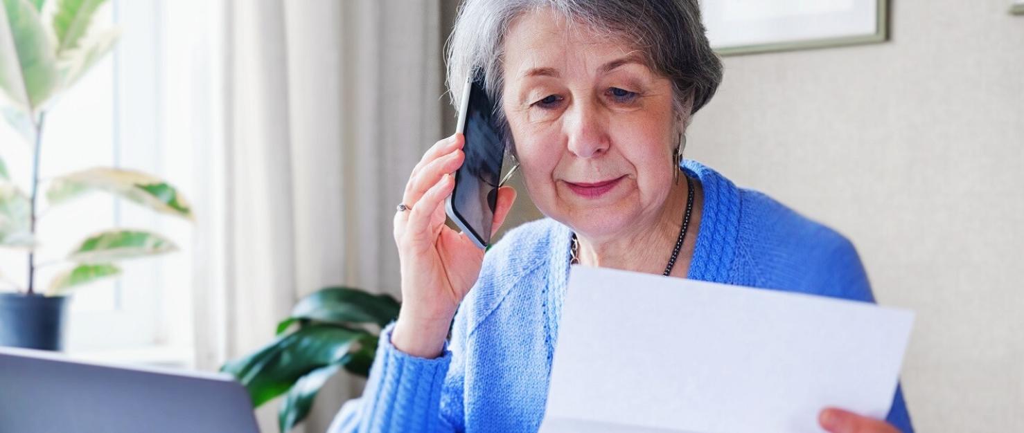 Vrouw bekijkt papieren met telefoon en laptop