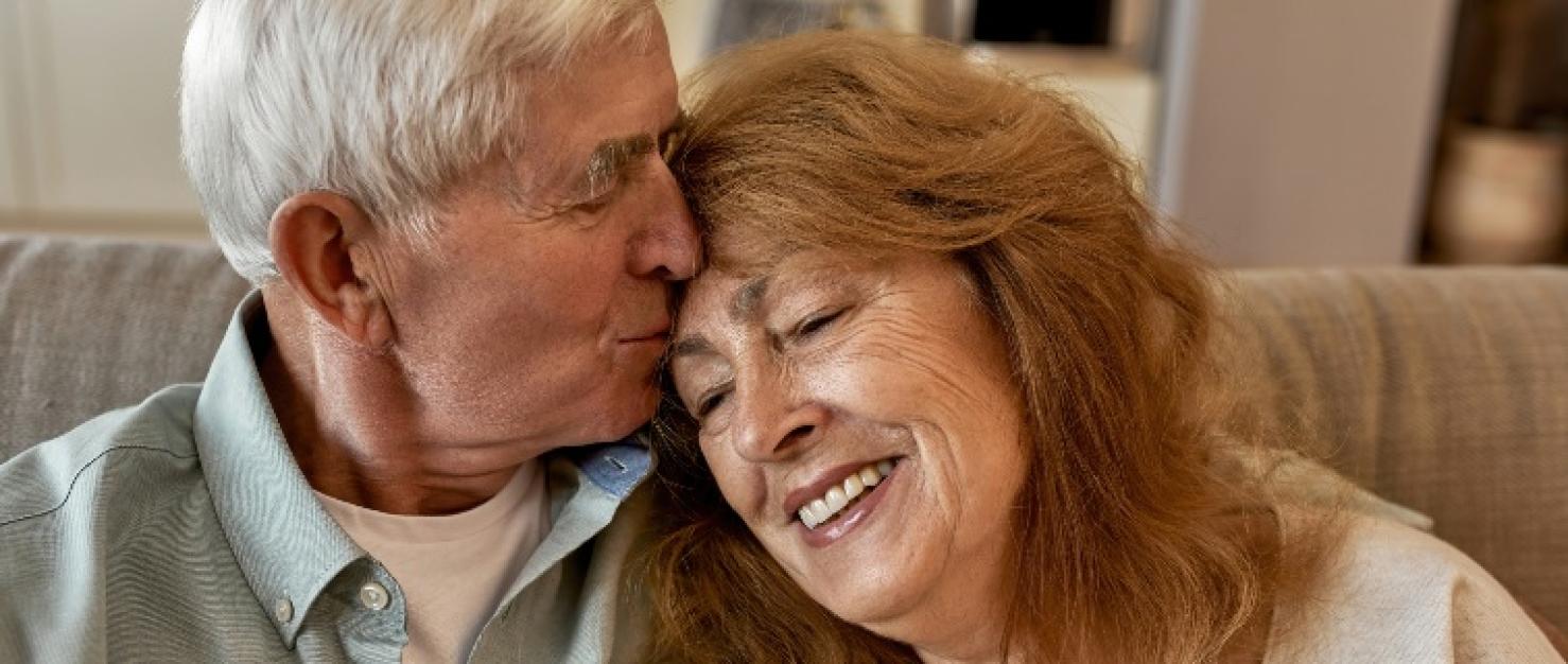 Ouder stel op bank, man kust voorhoofd vrouw